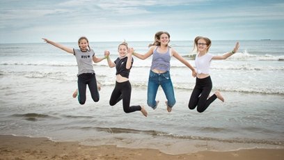 Vier Kinder springen gemeinsam nebeneinander am Strand in die Luft.