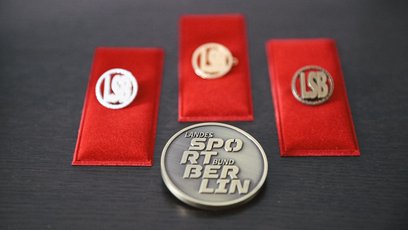 3 Ehrennadeln in Gold, Silber und Bronze werden präsentiert. Eine Medaille vom LSB Berlin liegt im Vordergrund.