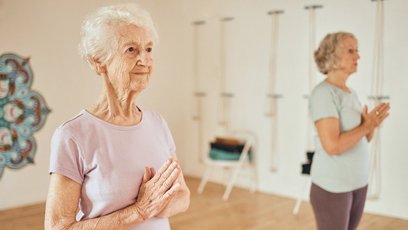 Zwei ältere Frauen bei einer Yogaübung mit gefalteten Händen