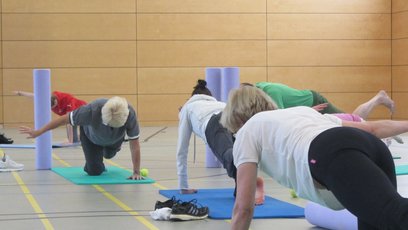 Personen machen in einer Sporthalle Übungen zur Kräftigung der Rückenmuskulatur